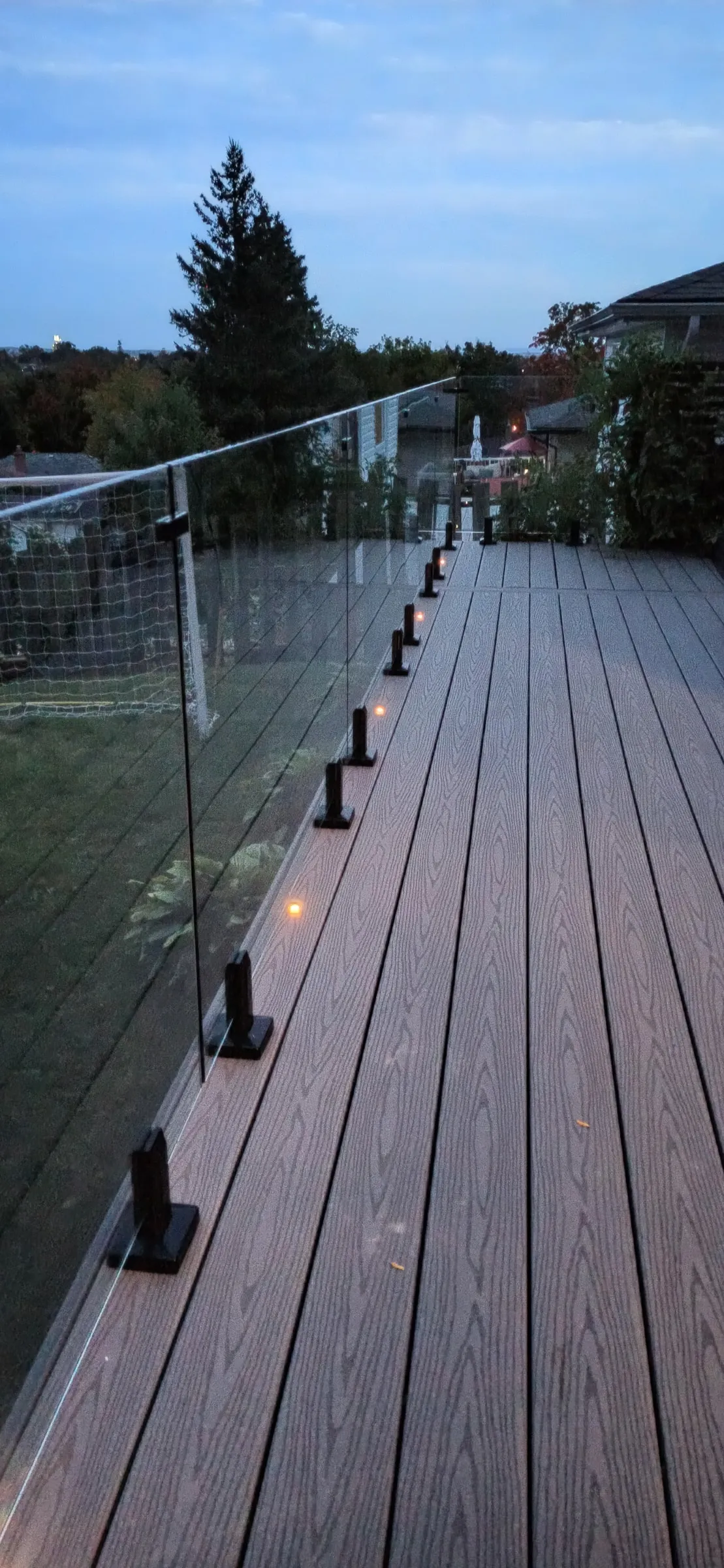 Small warm recessed lights mark the deck edge alongside glass railing at dusk