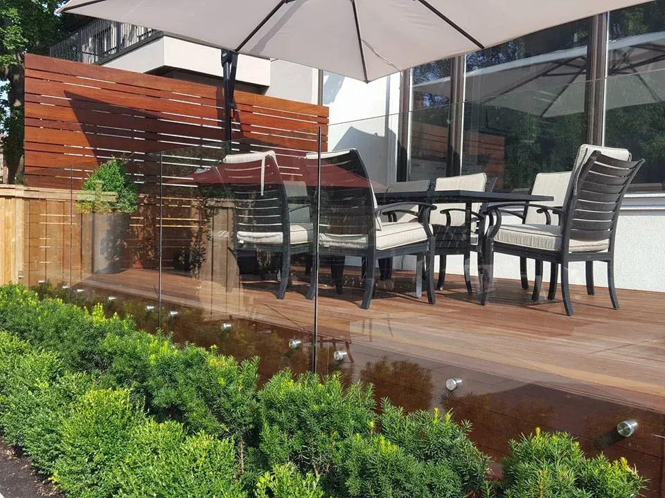 Ipe deck with clear frameless glass panels beside a wood privacy screen and outdoor dining furniture.