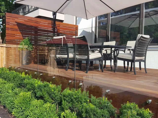 Ipe hardwood deck with outdoor dining, frameless glass railing, and a wood privacy screen