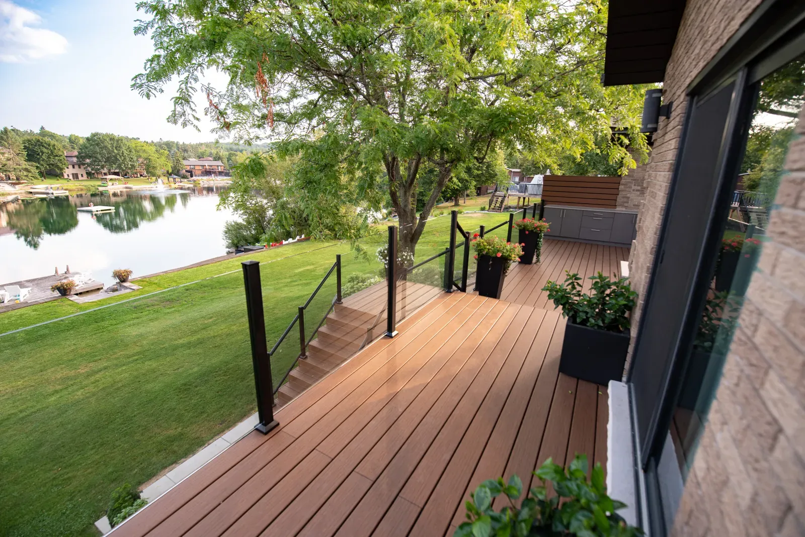 Warm brown composite deck with glass railings overlooking a lake.