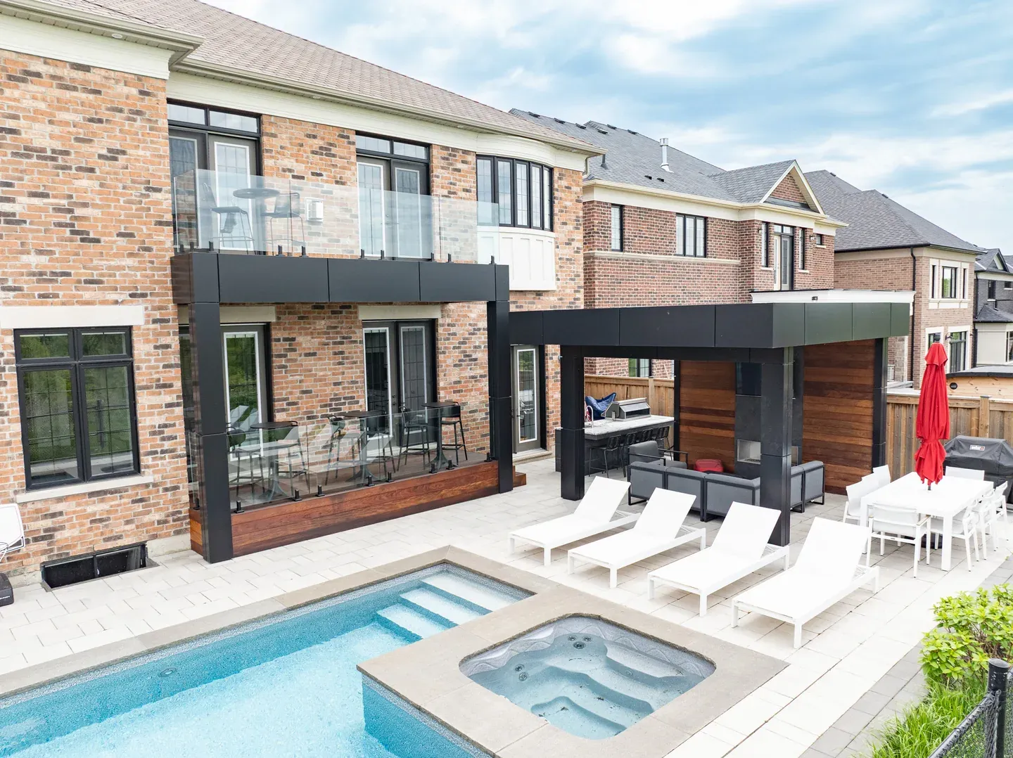 Poolside home with a wood deck, an upper glass-railed terrace and a dark-framed covered seating area.