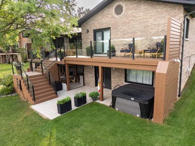Finished two-level composite deck with glass railings, stairs, and a hot tub on an Ontario home