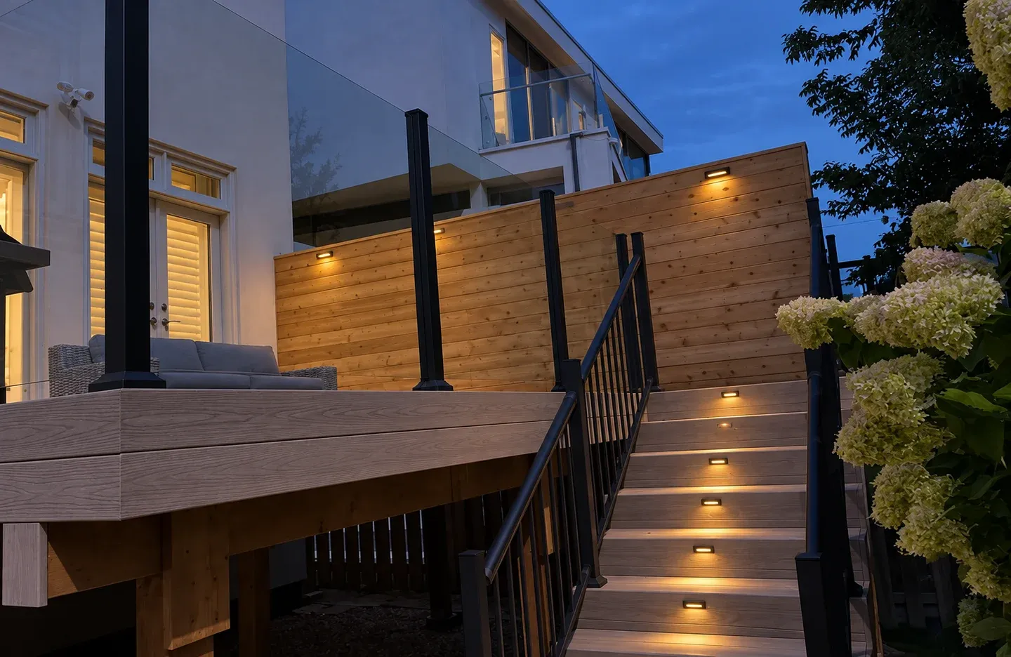 Warm lights in stair risers illuminate the treads beside a cedar privacy screen at dusk; lighting visualization based on a real project