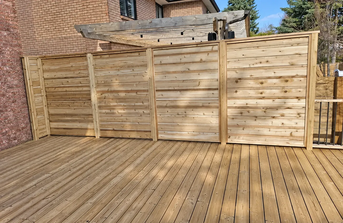 Pale, low-knot softwood deck boards with matching horizontal privacy screens on a completed backyard project